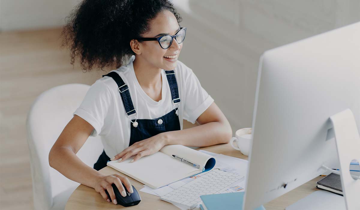 A young woman sitting at a desk working on a computer at a coworking space.